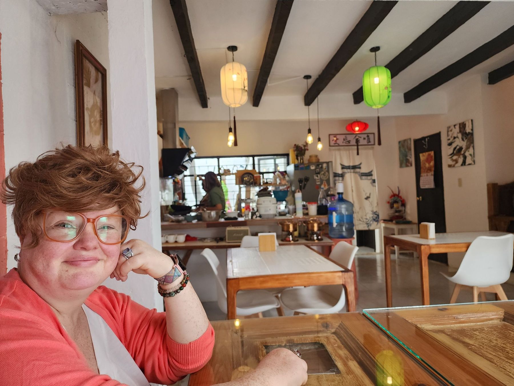 Renee Shupe smiling in a coral cardigan at a café table under paper lanterns
