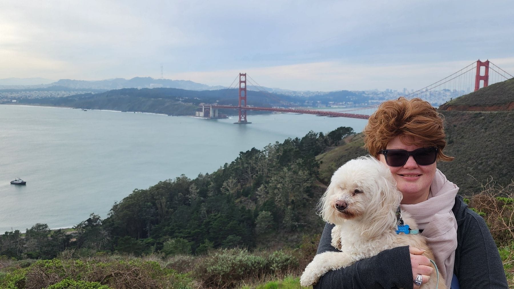 Renee Shupe holding her small white dog above the Golden Gate Bridge