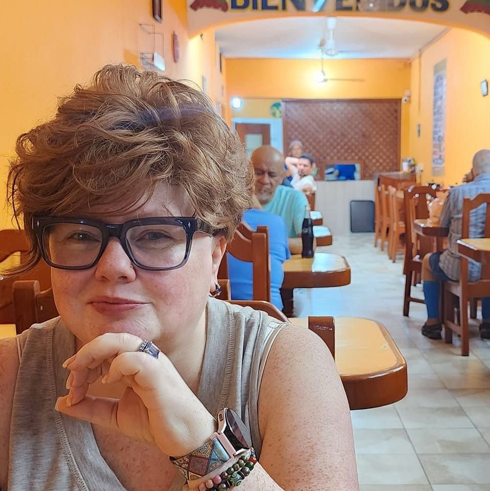 Renee Shupe smiling, chin on hand, in a sunny cafe