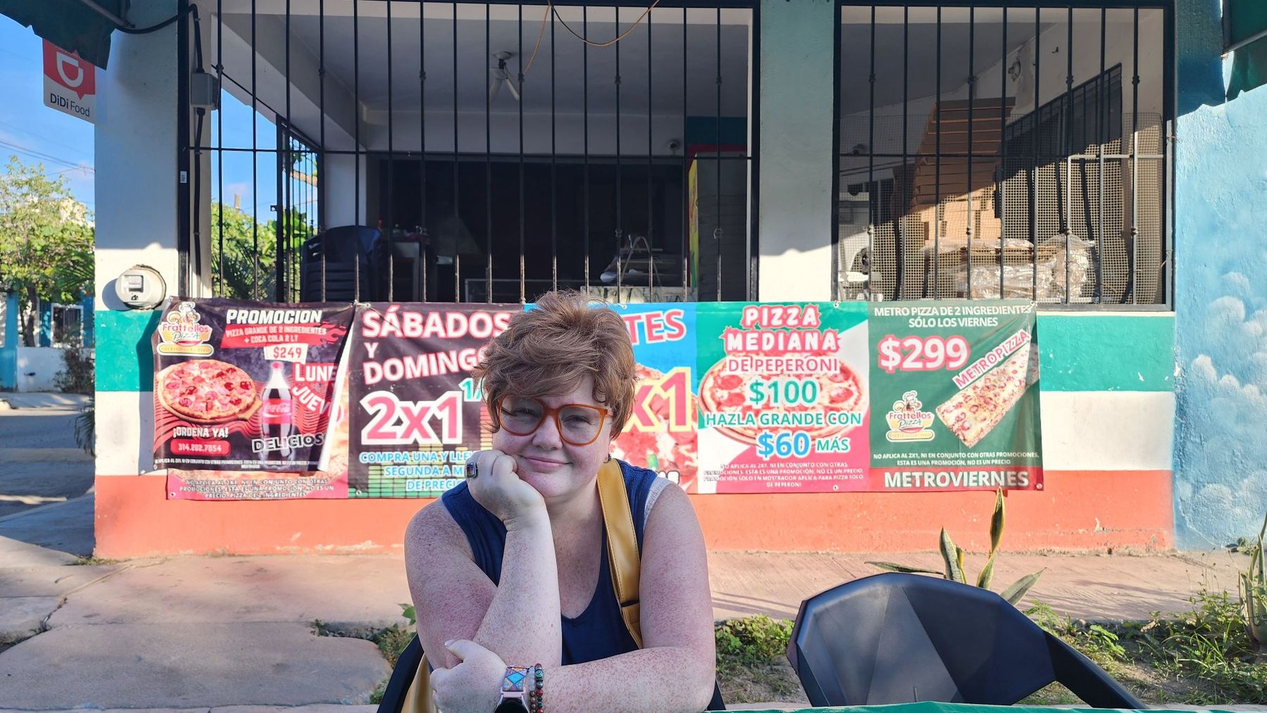 Renee Shupe sitting at an outdoor table in front of colorful pizza banners in Mexico